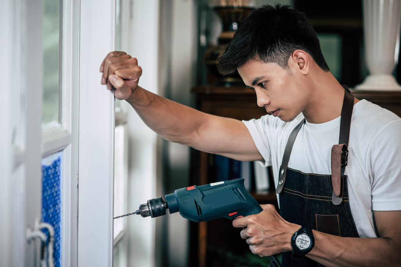 A handyman with a drill repairing a white graage door