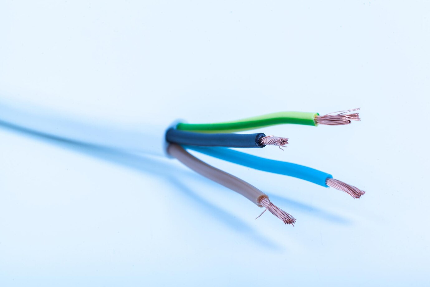 Close-up image of four exposed electrical wires with copper strands visible at the ends, covered in green, black, blue, and brown insulation, set against a light blue background