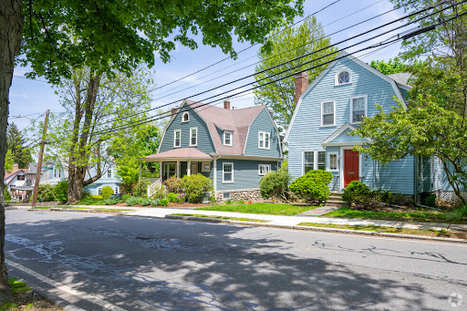 a serene residential street in Belmont, MA, showcasing charming, traditional houses with lush green surroundings, typical of suburban neighborhoods