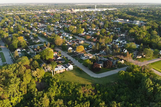 aerial view of Dedham, MA, showcases a suburban neighborhood surrounded by lush greenery. The image highlights tree-lined streets, residential homes, and a mix of open spaces and urban development