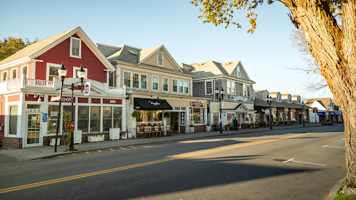 Charming street view in Falmouth, MA, featuring quaint shops, colorful buildings, and a tree-lined road