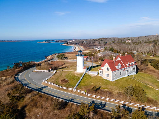 Aerial view of a lighthouse and coastline in Falmouth, MA, with a scenic road and surrounding natural landscape