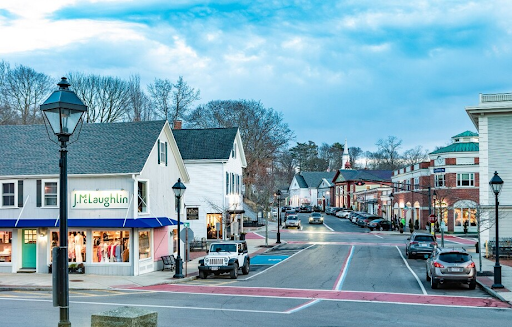 a charming downtown area in Hingham, MA, showcasing boutique shops, including a J.McLaughlin storefront, under soft evening light