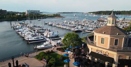 marina in Hingham, MA, featuring a docked fleet of boats and yachts against the backdrop of calm waters and distant green landscapes