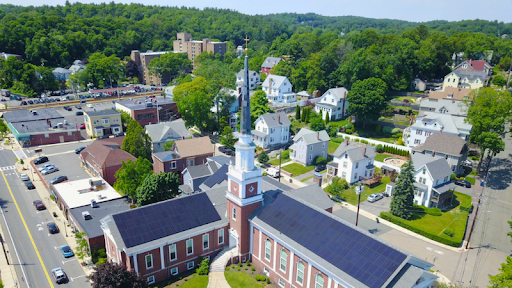 Aerial view of Melrose, MA, featuring a central church with solar panels, residential houses, and tree-lined streets in a suburban setting