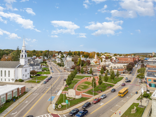 Aerial view of Milford, MA, highlighting the town's central park, surrounding streets with traffic, and a prominent white church with a steeple on the left