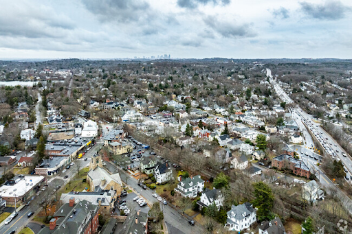 Aerial view of Needham, MA, showing residential neighborhoods, roads, and a distant city skyline