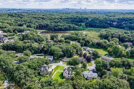 Aerial view of a residential area in Saugus, MA, surrounded by dense greenery, with Boston's skyline visible in the distance