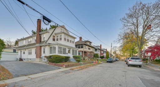 a residential street in Watertown Town, MA, characterized by a serene neighborhood with classic New England-style homes. The houses are well-maintained, featuring varied architectural styles, including porches, brick chimneys, and pitched roofs