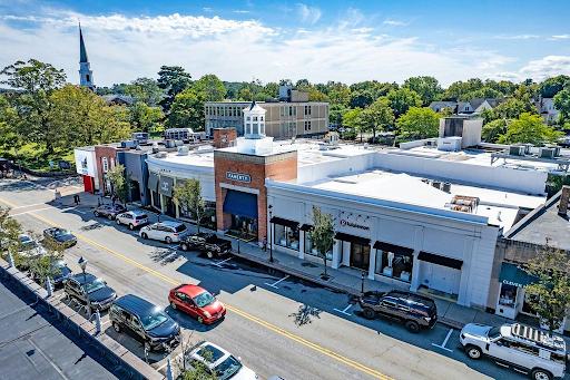 Aerial view of Wellesley, MA, showcasing a vibrant downtown area with shops, tree-lined streets, and a church steeple in the background