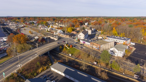 an aerial view of Wilmington, MA, featuring a mix of residential and commercial buildings. A bridge crosses over railroad tracks